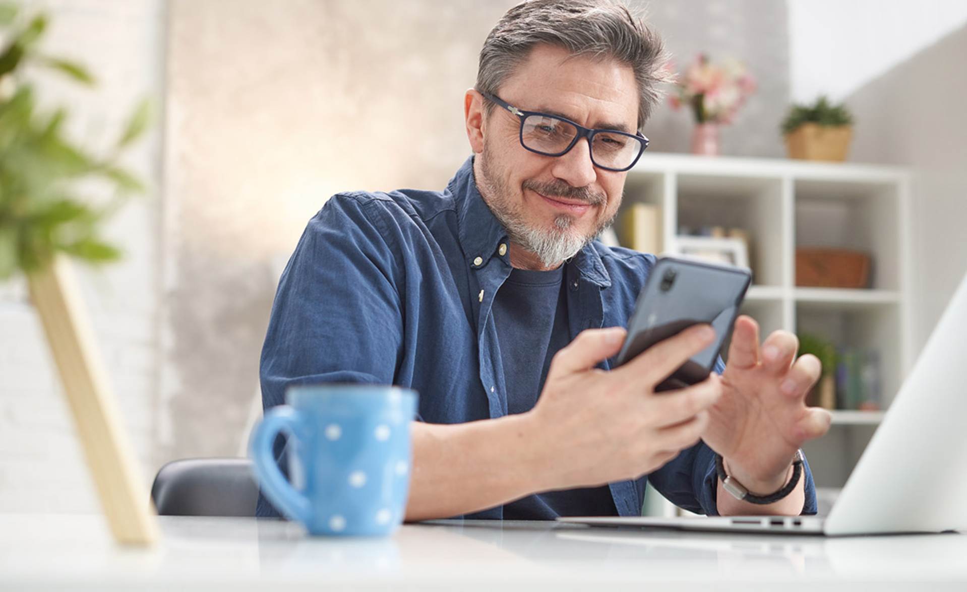 Mann sitz am Tisch und hält ein Handy in der Hand.