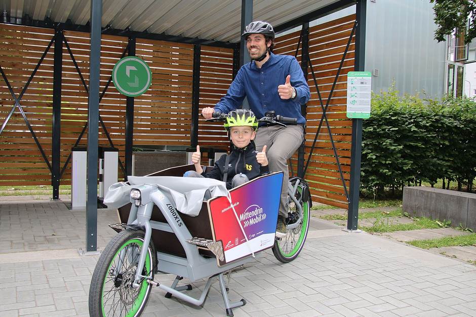 Mann sitzt auf einem Lastenrad und Kind sitzt darin.